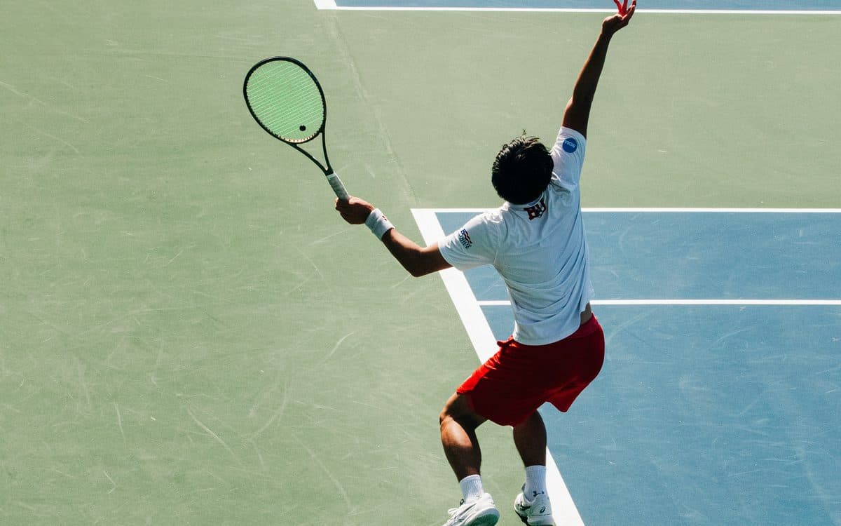 A tennis player mid-serve on a hard court